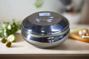 A stainless steel dish with a lid, displayed on a textured beige background.