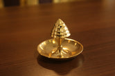 A brass agarbatti stand with a conical shape and a floral pattern on the top, placed on a wooden surface.